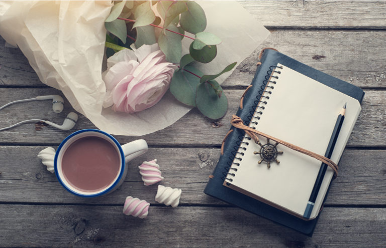 Pink ranunculus, open notebook, headphones on dark wooden background. Pastel colors, greeting card, toned vintage